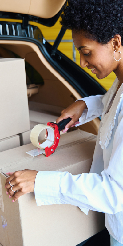 Vrouw met krullend haar plakt een verhuisdoos dicht.